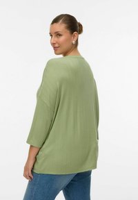 Haut oversize vert clair à manches trois-quarts, avec une texture côtelée et des fentes latérales, associé à un pantalon en denim bleu.