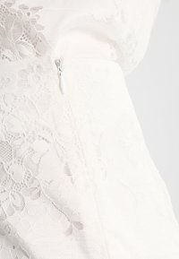 Weißes Spitzenkleid mit floralem Muster, strukturiertem Stoff, taillierter Silhouette und verdecktem seitlichen Reißverschluss zum Schließen.