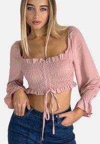 Rosa Cropped-Top mit geraffter Textur, Rüschensleeves und einem Bindeband in der Taille. Kombiniert mit dunkelblauen High-Waist-Jeans.
