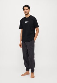 Must must värvi T-särk, millel on valge "BOSS" logo, koos mustade ja punaste triibuliste jogger-pükstega, millel on elastsed mansetid.