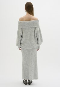 Ljusgrå, off-shoulder ribbad tröja och lång kjol. Mjuk textur, lös passform och långa ärmar. Svarta nätklackar fulländar looken.