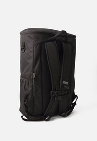 Zaino nero realizzato in tessuto resistente, dotato di spallacci imbottiti, tasca laterale con cerniera e schienale in rete per la ventilazione.