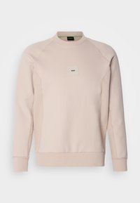 Sweat-shirt beige clair à manches longues et col rond, avec poignets et ourlet côtelés, présentant un petit patch logo "BOSS" centré sur la poitrine.