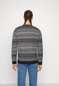 Pull en motif marine et crème avec un col rond et des poignets côtelés, présentant des motifs géométriques dans le dos. Porté avec un jean bleu.