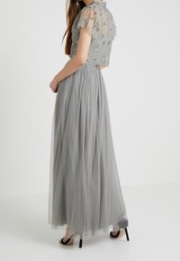 Graues Tüllkleid mit floralem Stickmuster, transparenten Kurzärmeln, einem taillierten Oberteil und einem fließenden Rock. Hat ein Punkte-Muster und ist knöchellang.