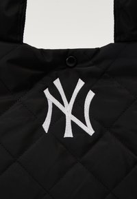 Bolsa tote acolchoada preta com um logótipo NY branco bordado, duas pegas e fecho com botão de pressão. Textura suave com padrão de diamante.