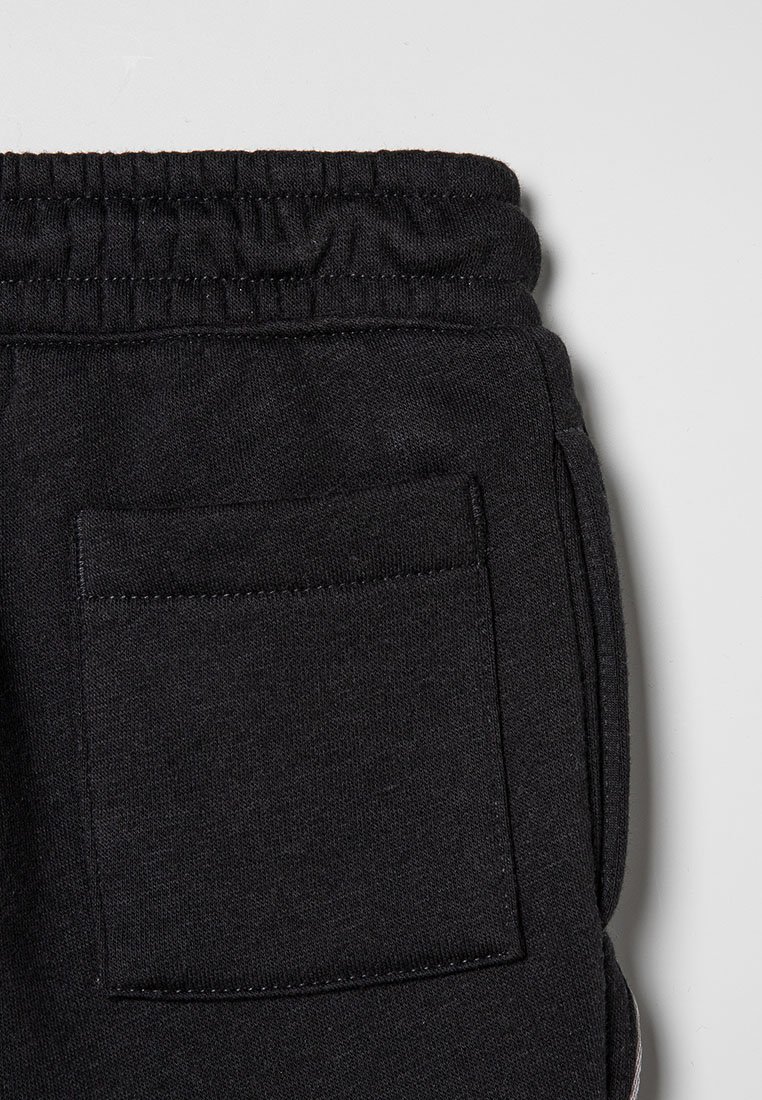 Schwarze Stoff-Sweatpants mit elastischem Bund und einer quadratischen Gesäßtasche, vor einem hellgrauen Hintergrund dargestellt.