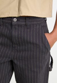 Svarte pinstripede bukser med klassisk design, som har gyldne sømmer, sidelommer og knappelukking i livet.