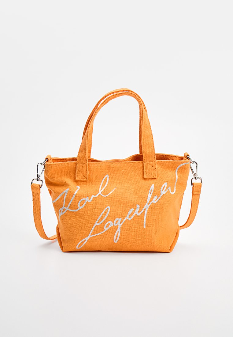 Oranje canvas handtas met twee handvatten en een afneembare schouderriem. Bevat witte cursieve tekst. Rechthoekige vorm met gestikte accenten.