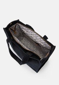 Bolsa de couro preta em cordura com fecho de zíper dourado, alças duplas e interior estampado com texto preto sobre fundo branco.