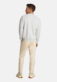 Sweat-shirt gris clair avec des poignets et un ourlet côtelés, associé à un pantalon beige et des baskets claires. Le tissu semble doux et texturé.