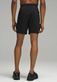 Svarta träningsshorts med elastiskt midjeband, som når till mitten av låret. Bärs tillsammans med svarta sneakers, vilket visar upp ett slätt tyg och enkel design.