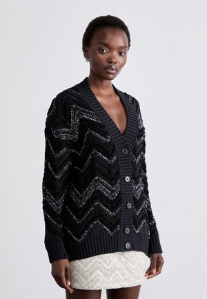 Cardigan noir avec un motif en chevrons, orné d'accents de sequins, de poignets côtelés et d'une fermeture à boutons sur le devant. Tissu texturé avec un décolleté en V profond.