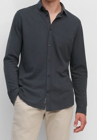 Dunkelblaues langärmeliges Hemd mit Button-Down-Kragen, das ein dezentes Logo auf der Brust und zwei Knöpfe an jedem Manschette aufweist. Aus Baumwollmischgewebe.