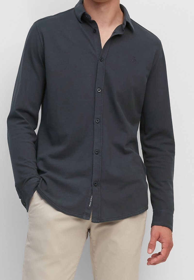 Dunkelblaues langärmeliges Hemd mit Button-Down-Kragen, das ein dezentes Logo auf der Brust und zwei Knöpfe an jedem Manschette aufweist. Aus Baumwollmischgewebe.