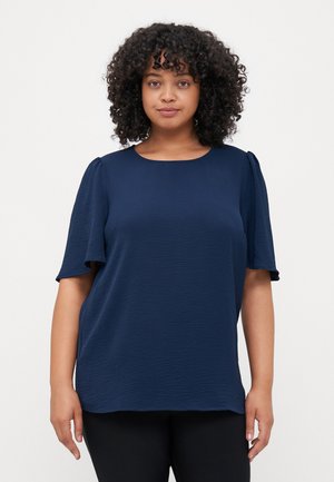 Navy blue short-sleeve top with a textured fabric, round neckline, and slightly puffed shoulders, worn over black pants.