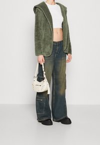 Grön, fuzzig jacka med huva, vit cropped topp och vida, bleka denimbyxor. Liten vit väska med metalldetaljer och dragkedja.