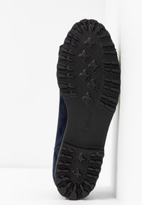 Semelle d'une chaussure marine avec un dessous en caoutchouc noir texturé, arborant un logo Gabor, positionnée sur un fond blanc.