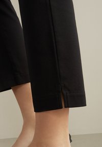 Svarta beskurna byxor i bomull med en mjuk textur och en sidoklyvning i fållen. Raka sömmar förbättrar designen.