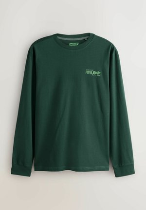 Langärmliges grünes T-Shirt aus Baumwolle. Mit rundem Halsausschnitt und einem grafischen Druck mit der Aufschrift "Paris.Berlin" in hellgrün.