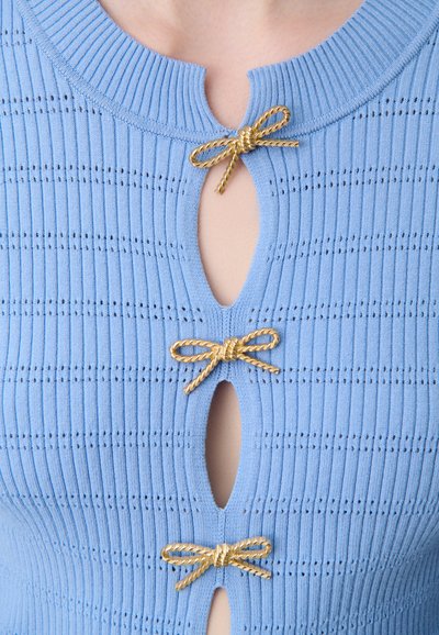 Top a costine azzurro chiaro con tre fiocchi in tono oro che accentuano aperture a chiave nel colletto, con una texture sottile e perforazioni.