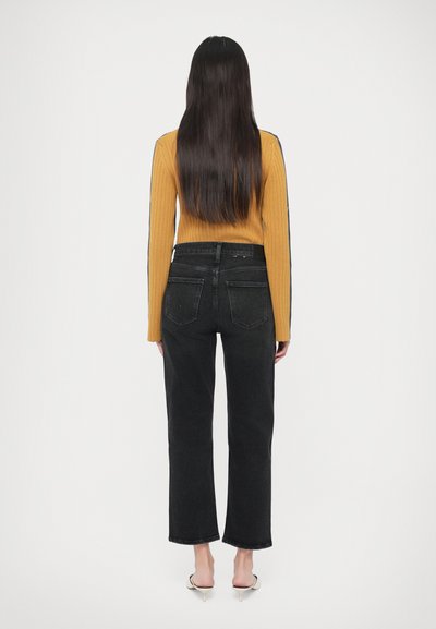 Μαύρο τζιν ψηλόμεσο, συνδυασμένο με μουσταρδί πλεκτό πουλόβερ με ανάγλυφη υφή. Το τζιν έχει ίσια γραμμή και πίσω τσέπες. Λείο ύφασμα.