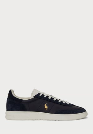 Mørkeblå lær- og semsket skinn sneakers med en hvit gummisåle, som har en gulllogo og hvite lisser, samt et strukturert design på overdelen.