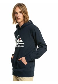 Navy hoodie featuring a front pocket, drawstring, and a large white and red logo. Soft, textured fabric with ribbed cuffs and hem.