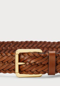 Pīta brūna ādas josta ar zelta metāla sprādzi un vienkāršu turētāju. Iezīmējas ar teksturētu virsmu un pītām apdarēm.