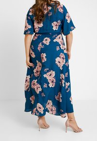 Blommig klänning med en teal bakgrund, prydd med stora rosa blommor. Flytande tyg, korta ärmar och ett åtsittande midja med en lång kjol.