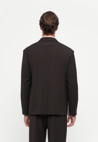 Blazer cu carouri de culoare maron închis, cu umeri structurați, rever în formă de notch și o deschidere pe spate. Prezentă două butoane la manșete și o etichetă de marcă.