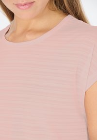 Vaaleanpunainen lyhythihainen paita, jossa on pehmeä, teksturoitu materiaali vaakasuorilla raidoilla ja pyöreä pääntie. Yksinkertainen, minimalistinen muotoilu.