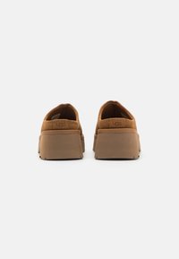 Scarpe slip-on in suede marrone con suola in gomma spessa e texture, e un design a profilo basso. Presentano un logo discreto sul tallone.
