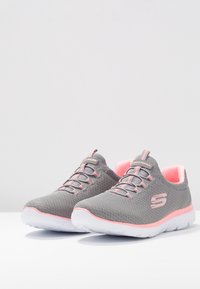 Szare buty sportowe z różowymi akcentami. Siatkowa cholewka z płaskimi sznurówkami, wyściełanym kołnierzem i kontrastującą białą podeszwą. Miękka wewnętrzna wyściółka.