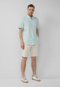 Korte mouwen, lichtblauw geruit shirt met een voorzak, gecombineerd met crèmekleurige shorts en crèmekleurige sneakers met neutrale accenten.