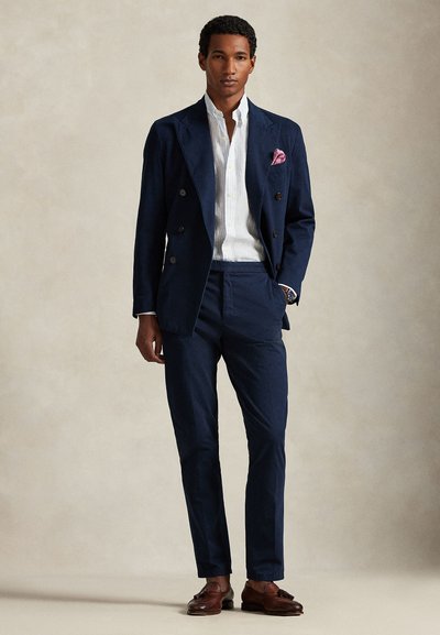 Μπλε διπλό breasted σακάκι, λευκό πουκάμισο με λεπτές ρίγες, μπλε παντελόνια, καφέ δερμάτινα παπούτσια και ροζ μαντήλι τσέπης. Λείο ύφασμα με εφαρμοστή ραφή.