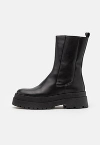 Botas de cuero negro hasta el tobillo con un diseño elegante, paneles laterales elásticos y suelas de goma gruesas con ranuras para tracción.