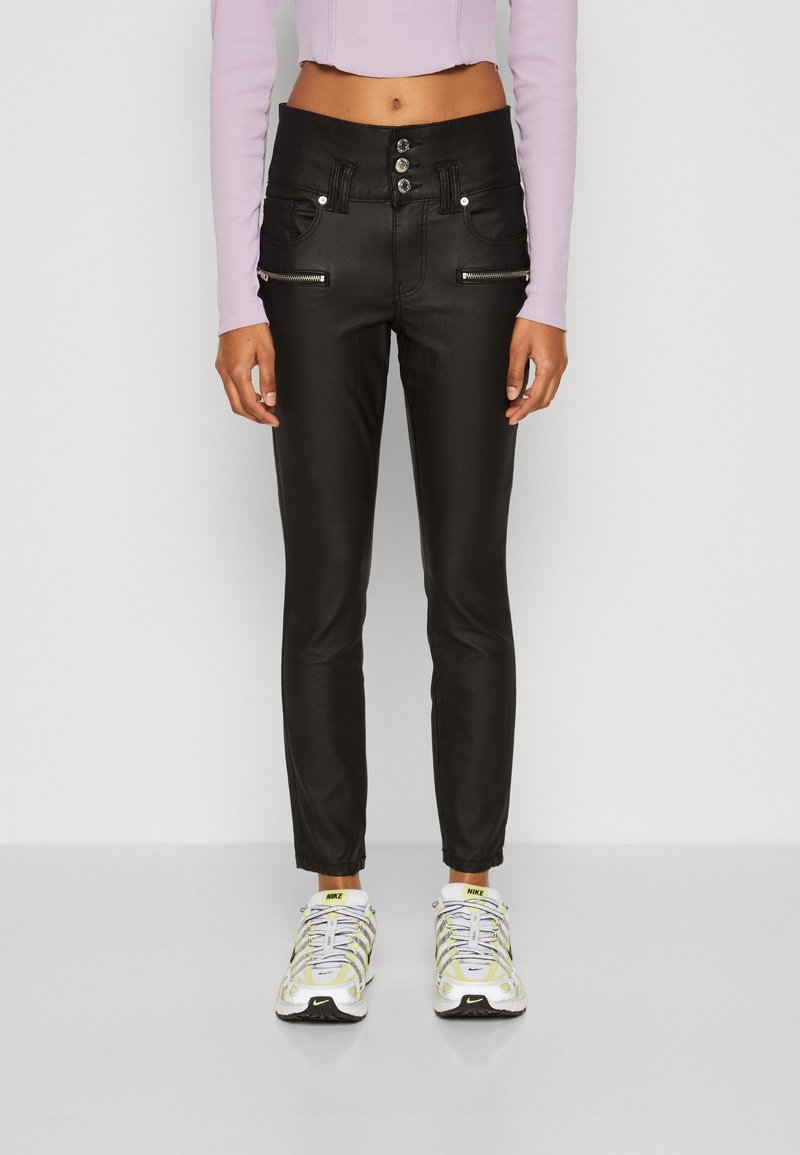 Czarne dopasowane spodnie z wysokim stanem, z zapięciem na trzy guziki i kieszeniami zapinanymi na zamek. W zestawie z lawendowym topem crop i białymi sneakersami.