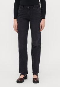 Juodi džinsai su tiesiomis kojomis, penkiais kišenėmis ir mygtuko uždarymu. Dėvimi su tamsiai rudos spalvos platforminiais bateliais.