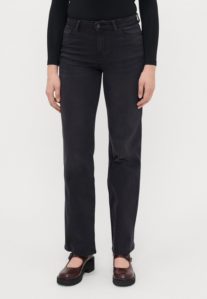 Juodi džinsai su tiesiomis kojomis, penkiais kišenėmis ir mygtuko uždarymu. Dėvimi su tamsiai rudos spalvos platforminiais bateliais.