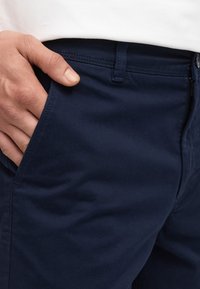 Pantalon bleu marine en mélange de coton, avec une poche latérale et des détails de couture visibles, au toucher lisse et à la coupe ajustée.