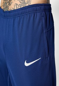 Nike træningsbukser i dyb blå stof med en glat tekstur. Har en elastisk talje, sidelommer og en hvid logo accent.