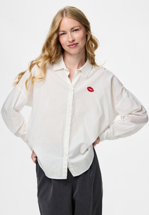 Camisa blanca de botones de tela ligera, con un sutil bordado de labios rojos en el lado izquierdo y un corte holgado y relajado.