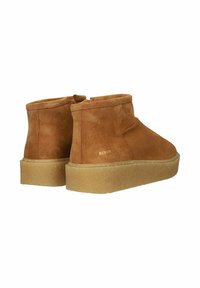Botas de ante hasta el tobillo en color beige, con una textura suave, punta redondeada, suela bicolor y cremallera en la parte trasera para ponérselas fácilmente. Acento de logotipo dorado.