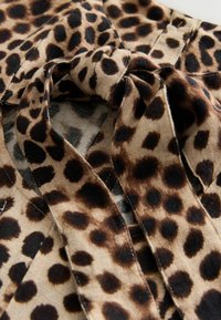 Nahaufnahme eines beigen Stoffes mit dunkelbraunen Leopardenflecken, der zu einem lockeren Knoten gebunden ist und dabei Textur und detailliertes Muster zeigt.