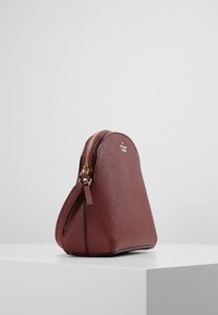 Bordeauxfarbene Lederhandtasche mit runder Form, goldenen Reißverschlussdetails und subtiler Textur. Verfügt über einen oberen Reißverschluss und einen flachen Boden.