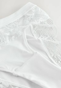 Witte lingerie van een gladde stof met kant langs de randen, voorzien van ingewikkelde bloemenpatronen en een zachte textuur.