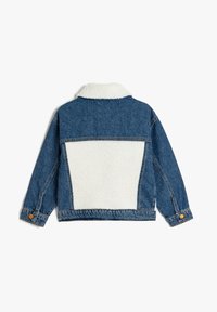 Chaqueta de mezclilla con un panel de pelaje sintético blanco en la parte trasera, puños abotonados y cuello de punta. Presenta un corte recto y costuras visibles.