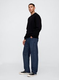 Schwarzer Rundhalsausschnitt-Pullover mit langen Ärmeln, kombiniert mit lockeren, dunklen Jeans und schwarzen Sneakers mit weißen Akzenten.