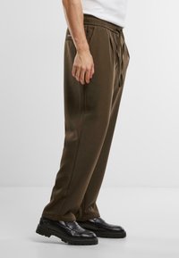 Pantalons marron, légers, avec taille élastique et cordon de serrage ; design à jambes droites ; portés avec des chaussures noires ; texture lisse.